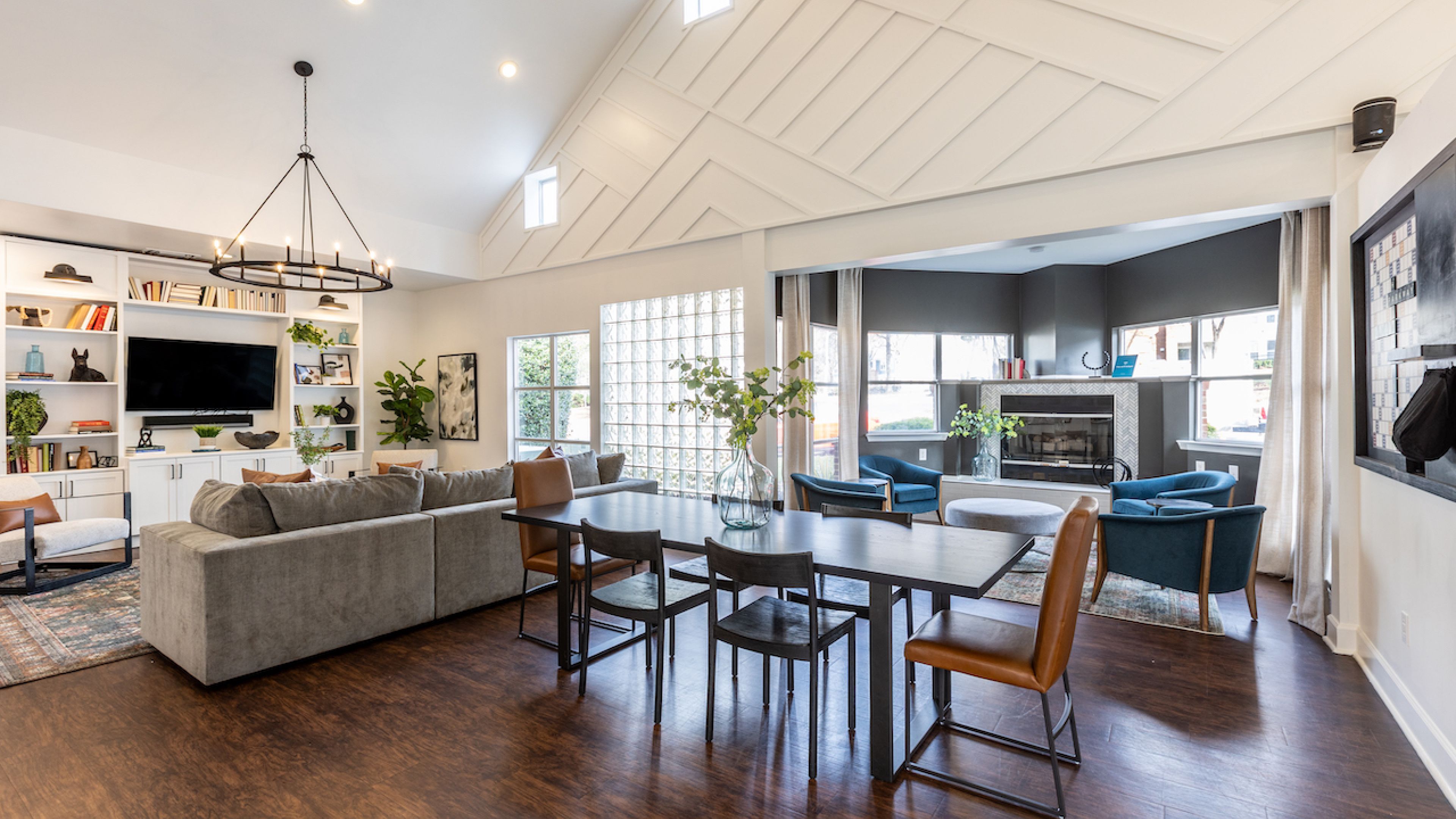 Hawthorne at the Parkway clubhouse of an apartment complex, featuring high vaulted ceilings, a spacious living area with a gray sectional sofa, and a dining area leading to a cozy fireplace lounge.