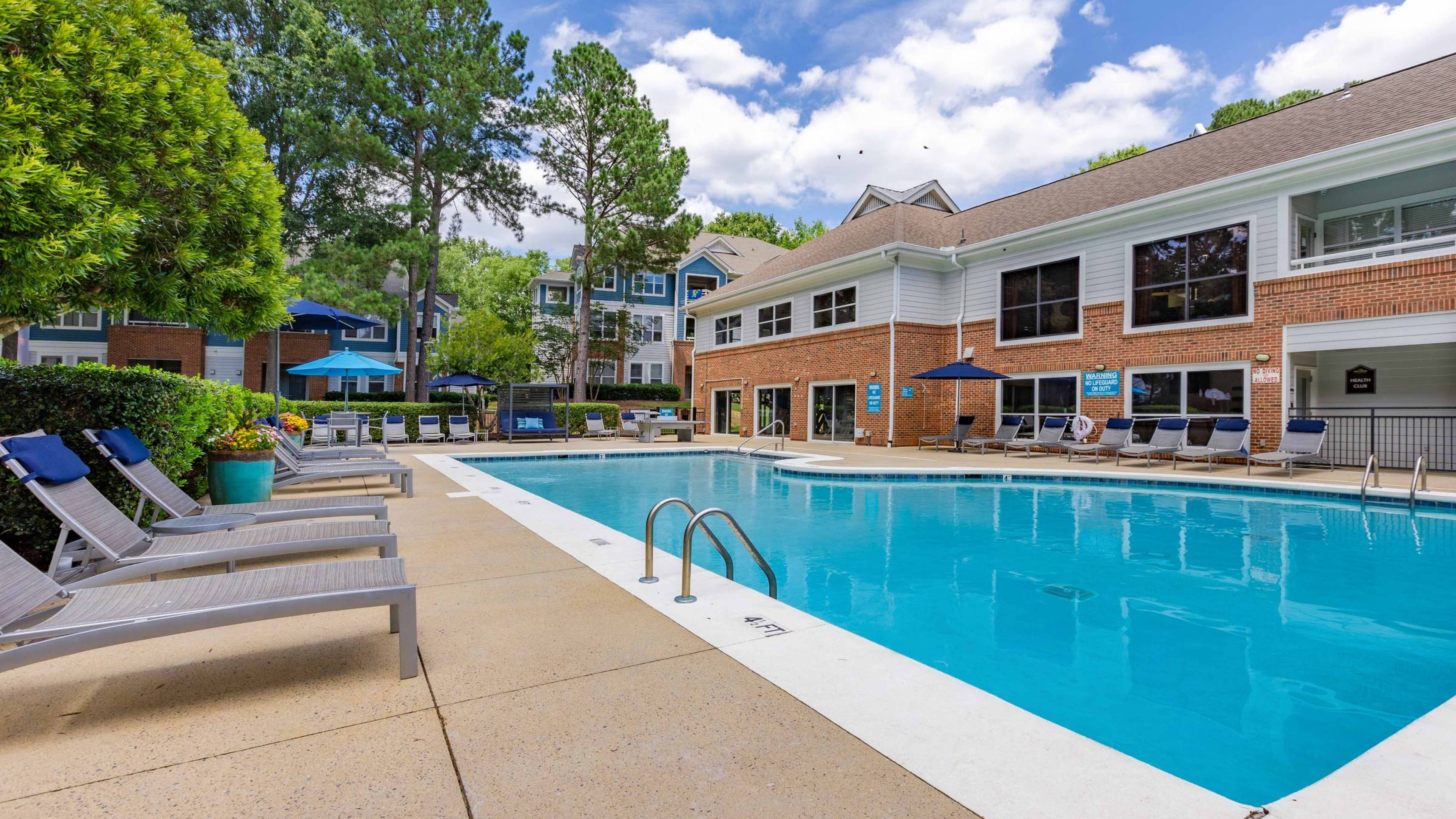 Hawthorne at the Parkway an inviting community swimming pool flanked by lounge chairs and surrounded by trees and apartments