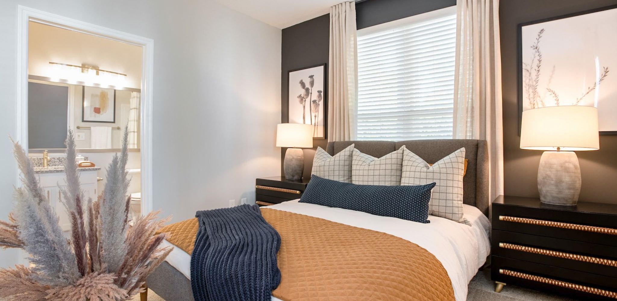 Hawthorne at the Parkway cozy bedroom featuring a plush bed with mustard and navy blue accents, flanked by elegant decor and warm lighting.